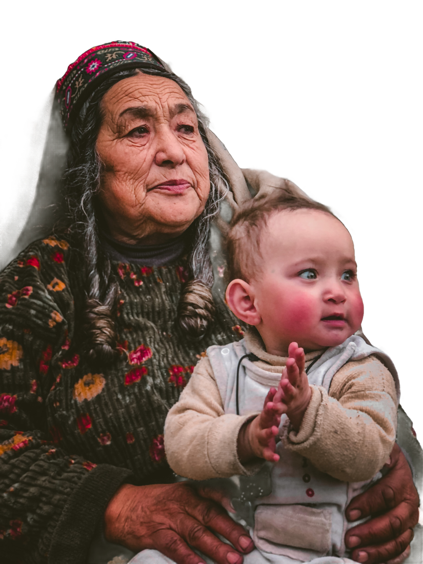 An elderly woman in a Hunza cap holds a baby on her lap