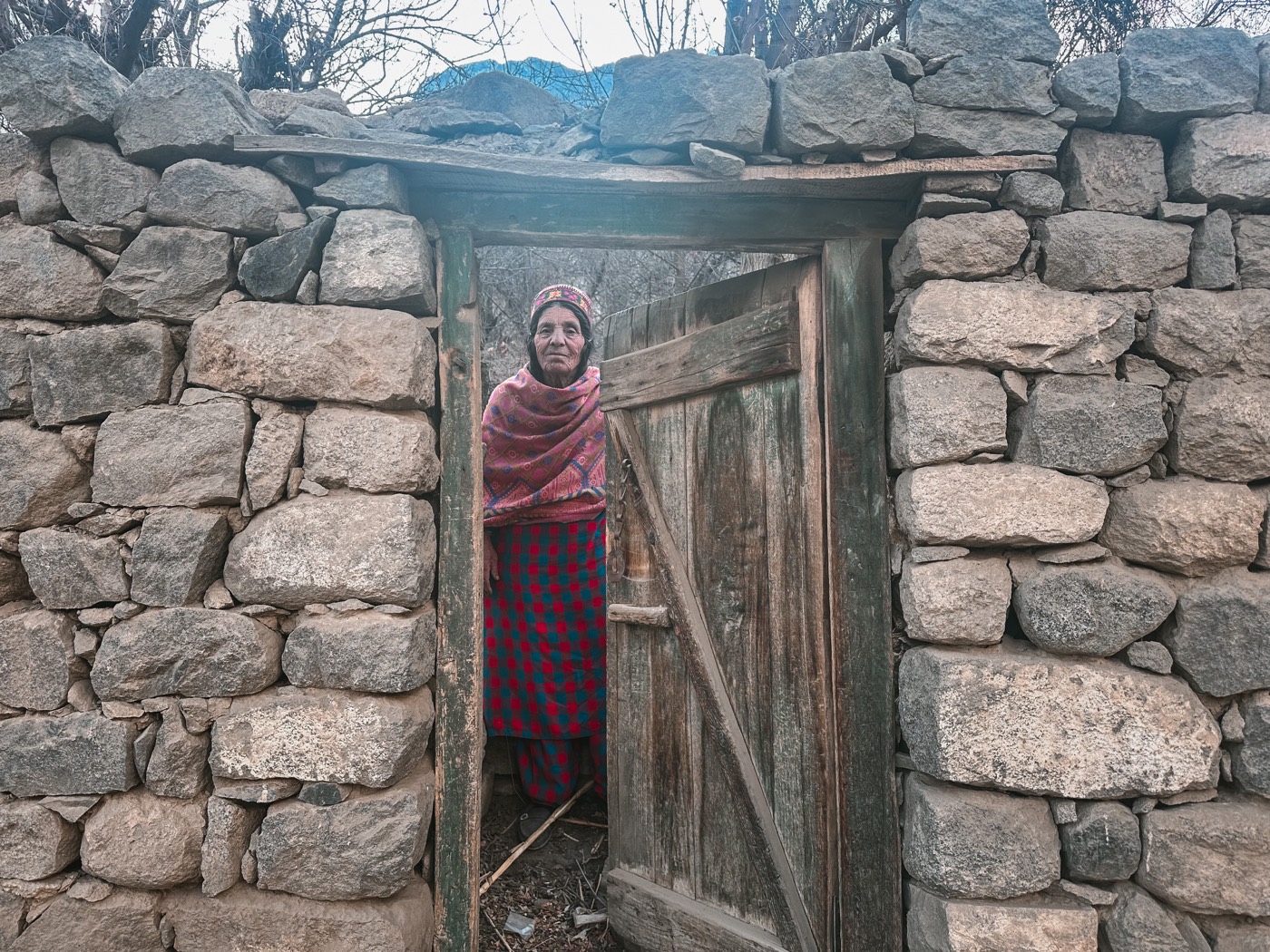 A woman standing in a wooden doorway set in a dry-stone wall